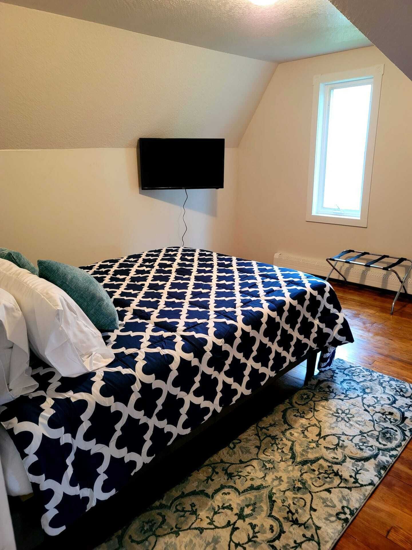 A bedroom with a bed, a TV mounted on the wall, a window, and a radiator.