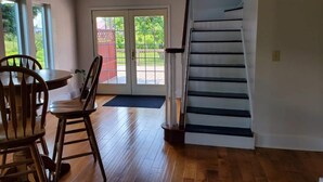 Un'ampia stanza con pavimento in legno, un'area pranzo con sedie e tavolo, una scala e una porta scorrevole in vetro che dà su uno spazio esterno.