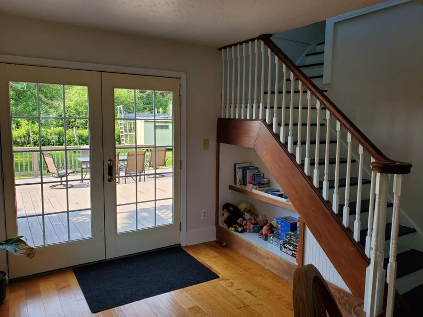 A home interior with a wooden staircase, a sliding glass door leading to a deck, and a bookshelf with toys.