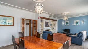 Ein modernes Wohnzimmer mit Essbereich, ausgestattet mit einem Holztisch, blauen Sofas und dekorativer Beleuchtung.