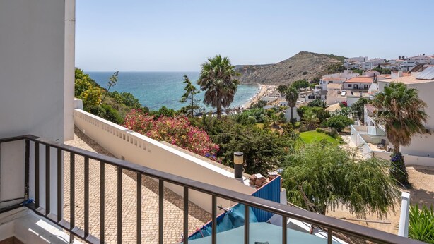 Ein Balkon mit Blick auf einen Strand, ein Schwimmbad und eine Stadt am Hang.