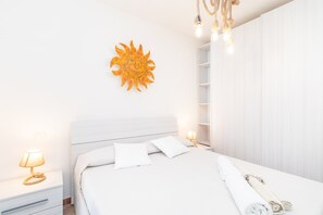 A bedroom with a bed, bedside lamps, a wall-mounted sun decoration, and a white wardrobe.