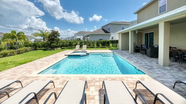 Une piscine avec des chaises longues, un patio couvert et une pelouse bien entretenue.