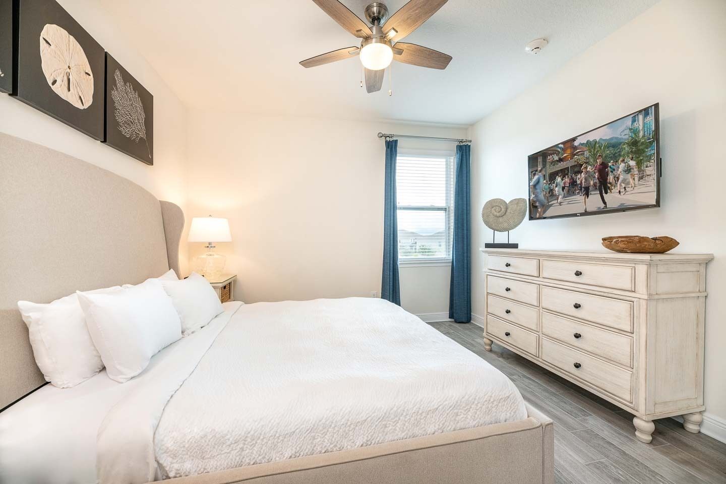A bedroom with a bed, a nightstand, a dresser, a ceiling fan, and artwork on the walls.