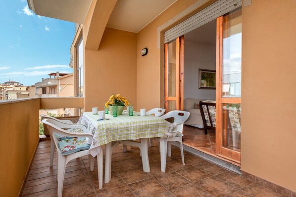 A balcony with a table set for two, chairs, and a potted plant.