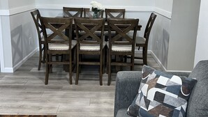 A dining area with a wooden table and chairs, a gray sofa with a patterned pillow, and artwork on the wall. - GOTL Strip Suite #3- Sunset Vacation Rentals (Geneva)