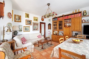 Una sala de estar con un sofá, una mesa de centro, una mesa de comedor, sillas y una estantería llena de libros y objetos decorativos.