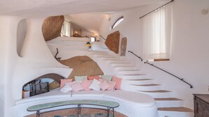 A modern interior with a curved staircase, a seating area with cushions, and a patterned rug.