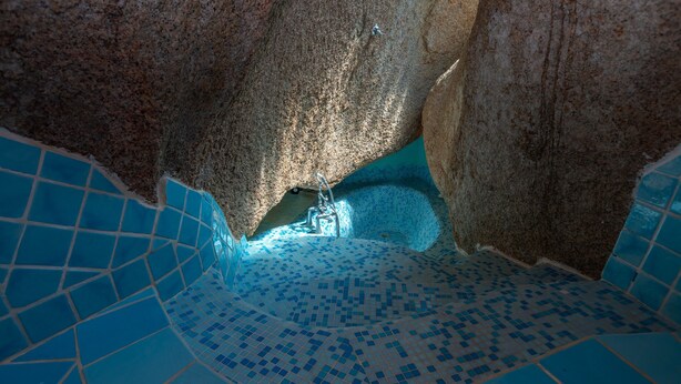 A tiled pool with a geometric pattern, a stone wall, and a metal ladder.