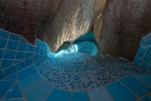 Ein mit geometrischen Mustern gefliester Pool, eine Steinmauer und eine Metallleiter.