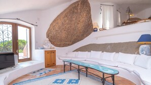 A living room with a white sofa, a coffee table, a large rock, and a TV.