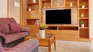 A living room with a sofa, a coffee table, a TV, and shelves with plants.