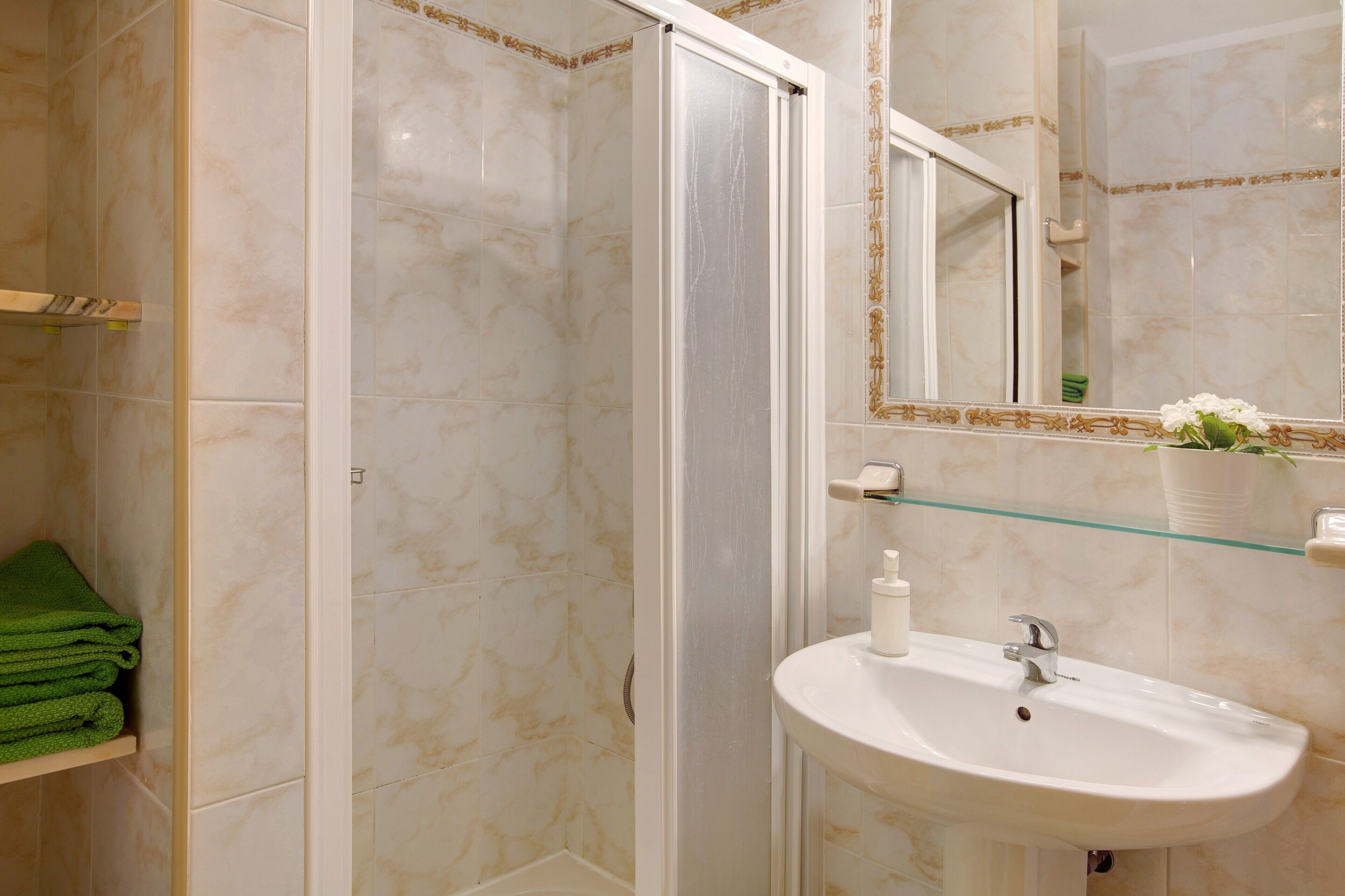 A bathroom with a glass shower enclosure, a sink with a mirror, and a green towel rack.