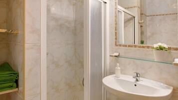 A bathroom with a glass shower enclosure, a sink with a mirror, and a green towel rack.