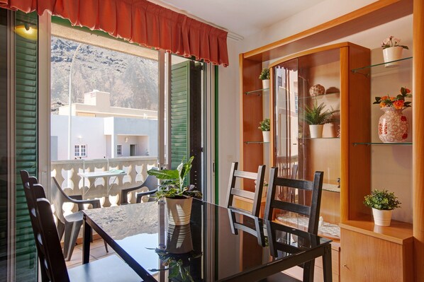 A dining area with a table and chairs, a glass partition, and a wooden cabinet with shelves.