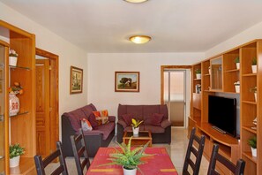 A living room with two sofas, a coffee table, a TV, and wooden shelving with plants.