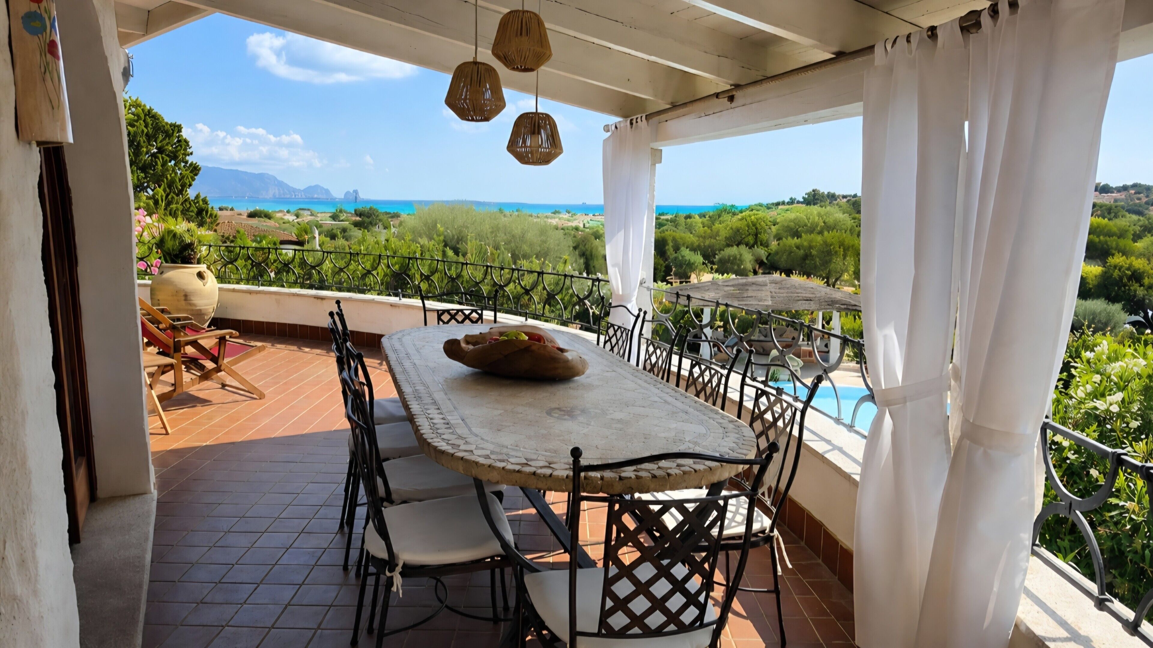 Eine Terrasse mit Tisch und Stühlen, mit Blick auf ein Schwimmbad und üppiges Grün.