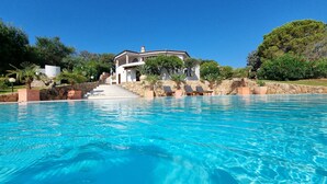 A swimming pool with lounge chairs, a stone wall, and a house with a stone staircase. - Villa LUNA ROSSA with Sea View, Pool, A/C, Wi-Fi, Garden, Terrace & Balcony (san teodoro)