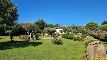 Un jardin bien entretenu, agrémenté d’un grand rocher en guise d’élément central, un bâtiment blanc doté d’un balcon et un ciel d’un bleu limpide.