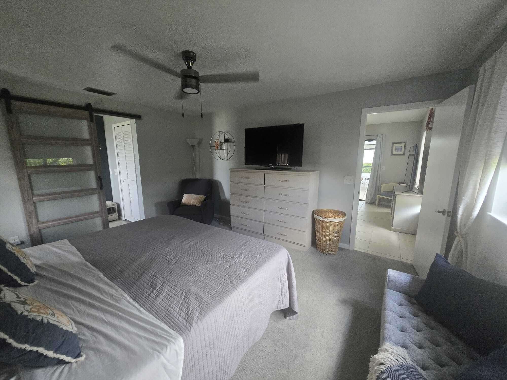 Une chambre à coucher comprenant un lit, une commode, un téléviseur, une chaise et un ventilateur de plafond.