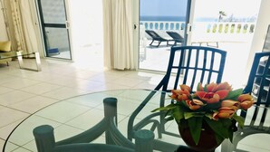 Una habitación con una mesa de vidrio, una planta en maceta y vistas al mar desde un balcón.