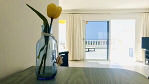 Un florero de vidrio transparente con una tulipa amarilla sobre una mesa de mármol en una habitación bien iluminada, con vistas a un balcón y una puerta que da al exterior.