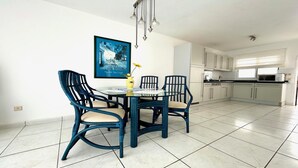 Un comedor con una mesa redonda y cuatro sillas, un cuadro en la pared y una cocina al fondo.