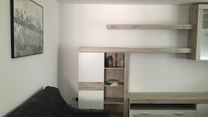 Una sala de estar moderna con un sofá de cuero negro, un mueble de madera con libros y objetos decorativos, y una fotografía en blanco y negro enmarcada en la pared.