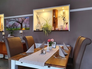 Un coin repas avec une table en bois, quatre chaises, un vase de fleurs et un tableau accroché au mur.