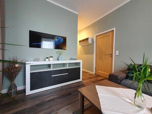 Un salon moderne avec un meuble de rangement blanc pour l’équipement audiovisuel, une table basse en bois, un canapé et une porte.