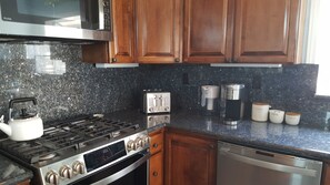 Una cocina con encimeras de granito y electrodomésticos de acero inoxidable, incluyendo estufa, microondas, tostadora, cafetera y lavavajillas.