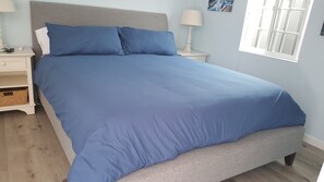 A bedroom with a large bed, a nightstand, a lamp, and a window.
