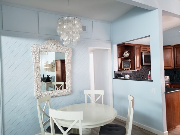 A dining area with a white round table, two white chairs, a decorative mirror, and a hanging light fixture.