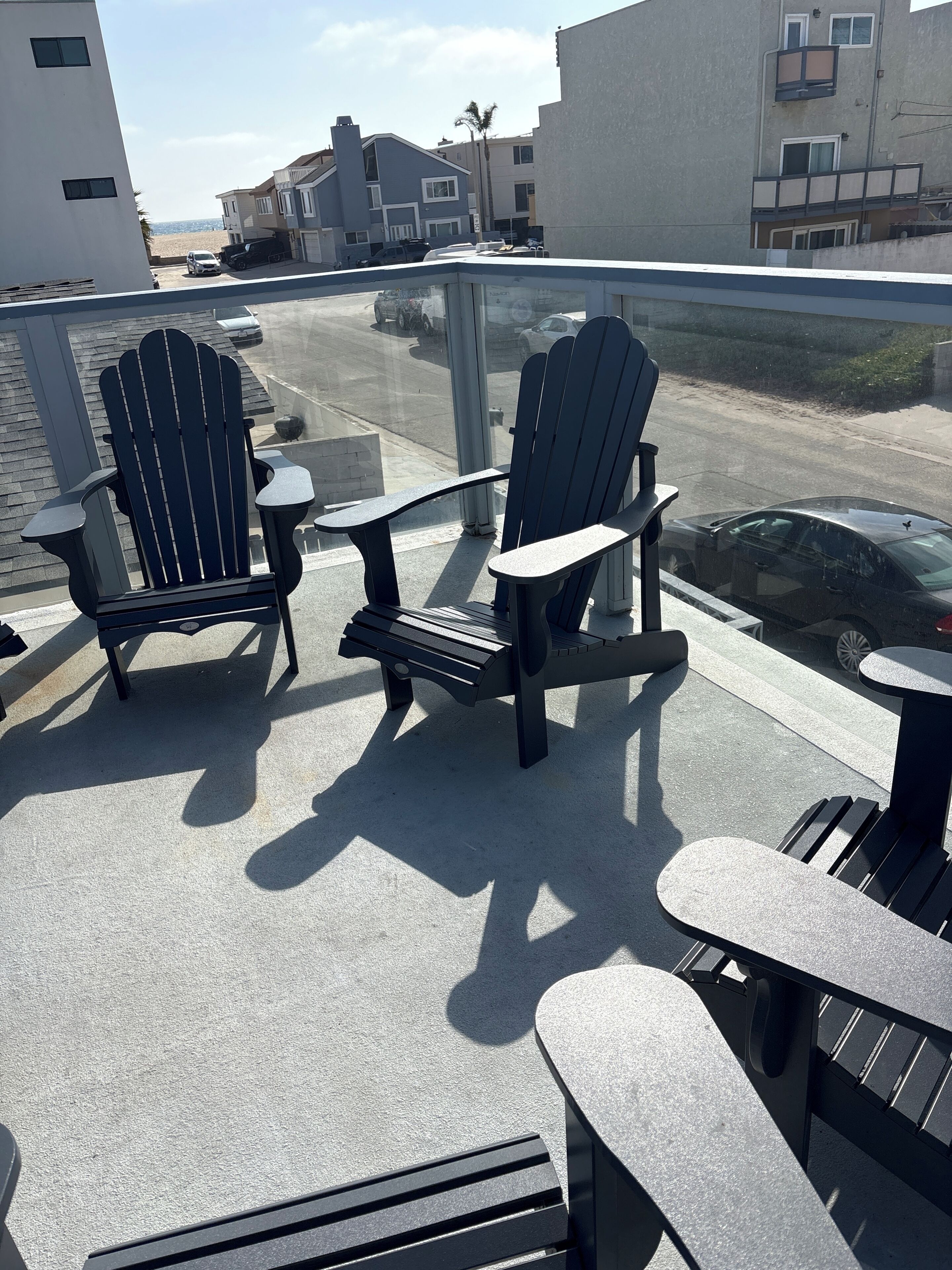 Two Adirondack chairs on a balcony with a view of the street and buildings.