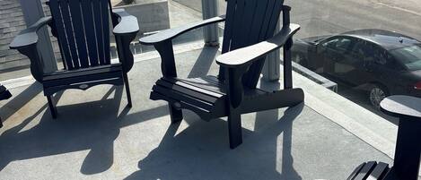Two Adirondack chairs on a balcony with a view of the street and buildings.