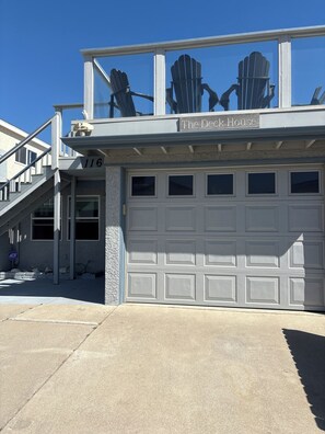 A residential property with a garage, a balcony with Adirondack chairs, and a clear blue sky. - The Deck House on the Silver Strand (Oxnard)