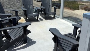 A balcony with Adirondack chairs, a view of a street with cars, and buildings in the background. - The Deck House on the Silver Strand (Oxnard)