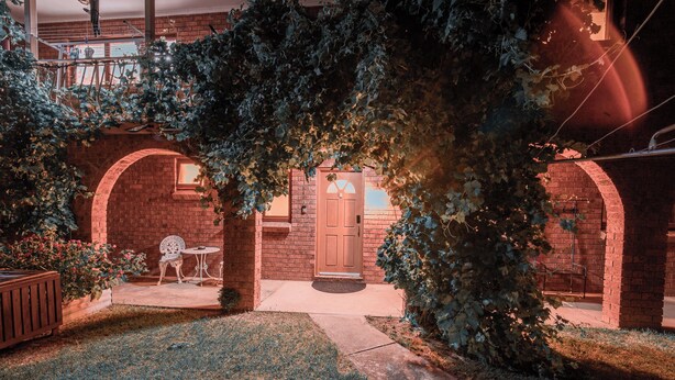 A brick house with a front door, a small porch with a chair and table, and a garden area. - Cooma home with fresh air and a mountain view (Cooma)