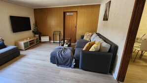 A living room with a sofa, a coffee table, a TV, and a door. - Cooma home with fresh air and a mountain view (Cooma)