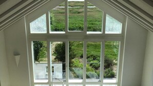 Una habitación con techo inclinado, ventanas amplias y vistas a un paisaje verde.