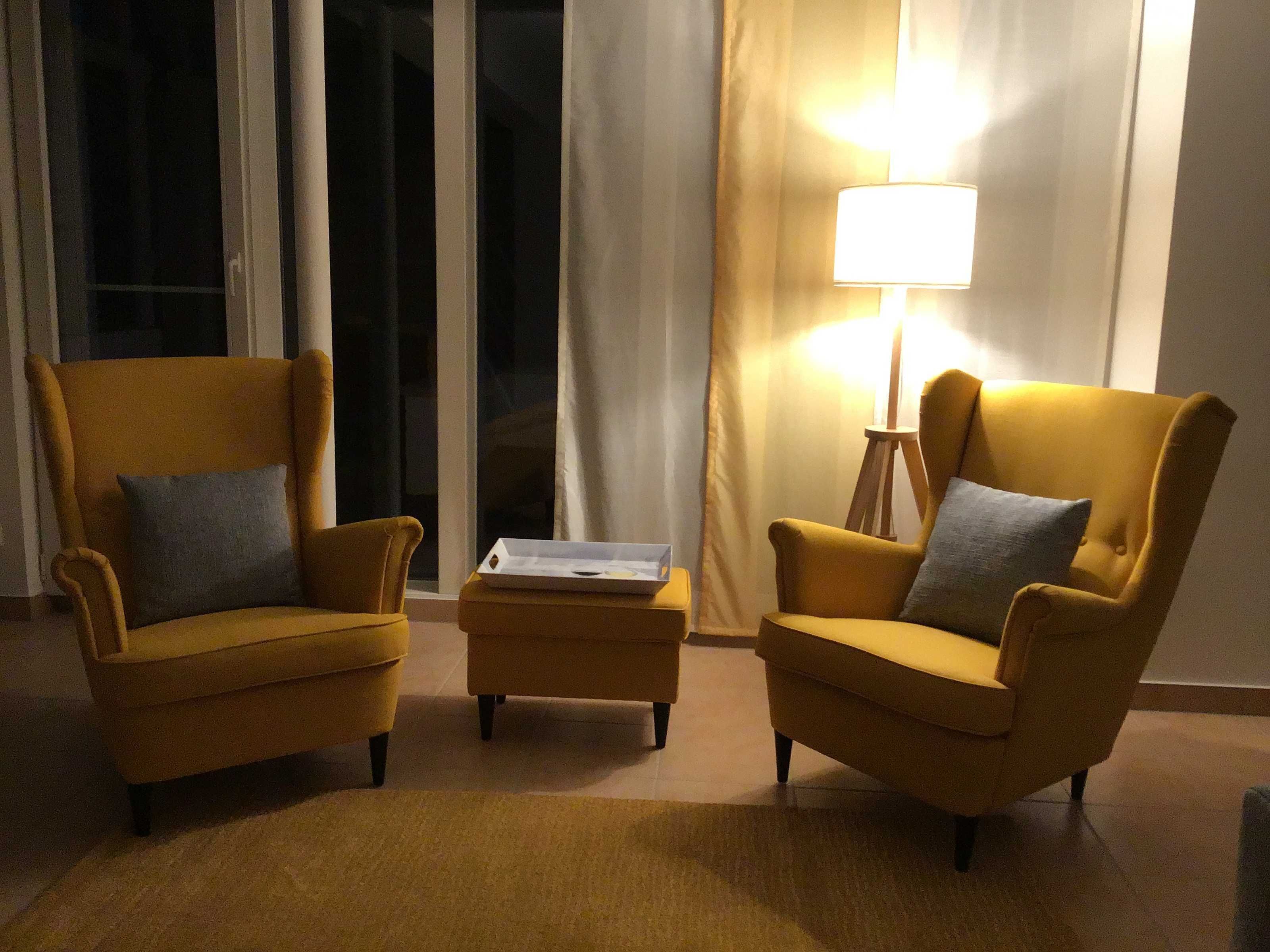A room with two yellow armchairs, a small ottoman, and a floor lamp.