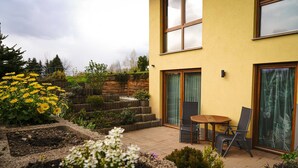 A modern house with a yellow exterior, a wooden deck, and a small patio area with a table and chairs. - Vacation apartment Hellerswiesen - Fewo Hellerswiesen (Bahretal)