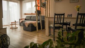 A living room with a sofa, a dining table with chairs, and a staircase with a plant on it. - Vacation apartment Hellerswiesen - Fewo Hellerswiesen (Bahretal)