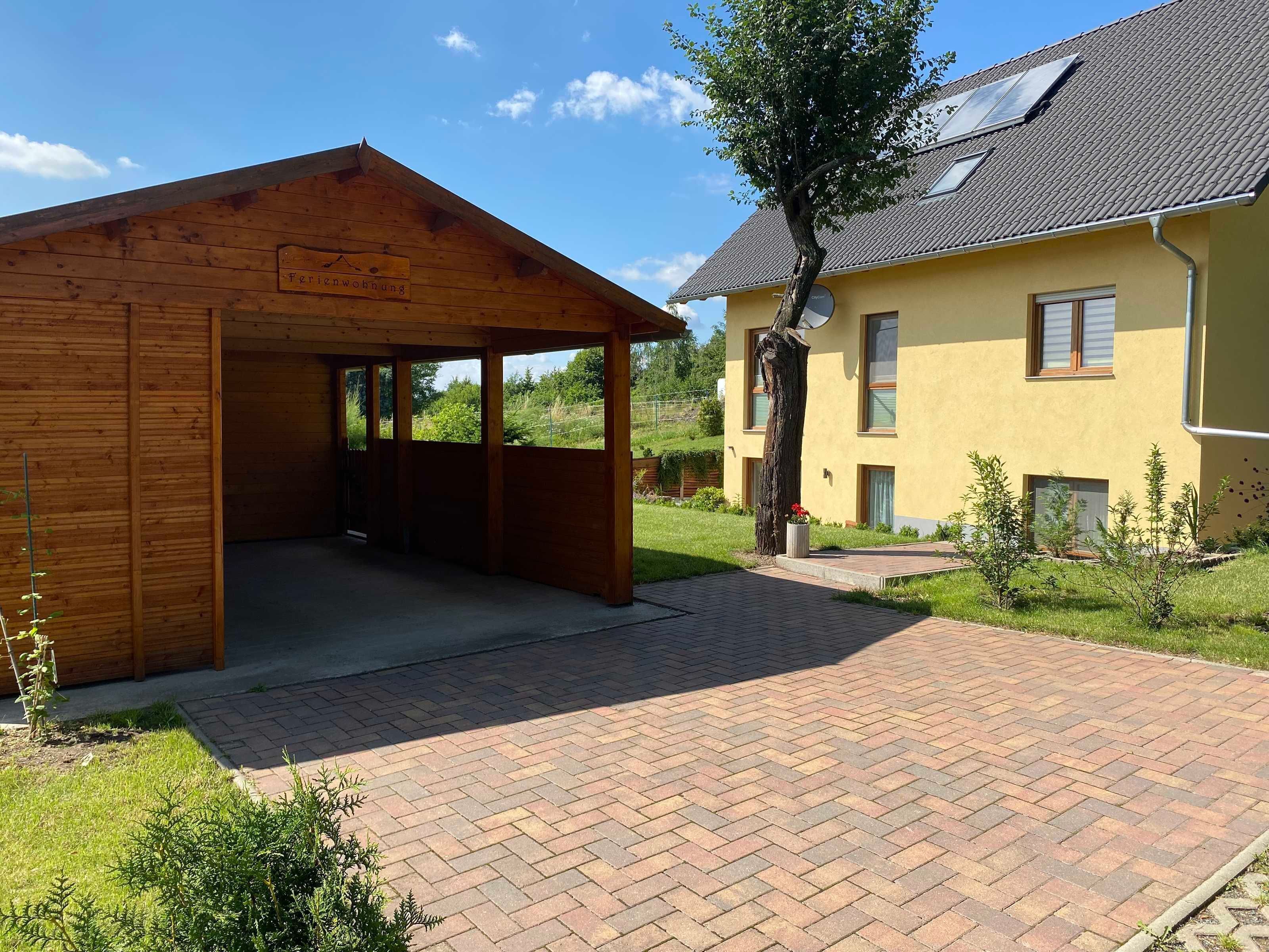 A wooden cabin with a covered porch, a yellow house with a tiled roof, and a brick pathway.
