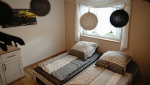 A single bed with patterned bedding, a bedside table, and a window with curtains. - Vacation apartment Hellerswiesen - Fewo Hellerswiesen (Bahretal)