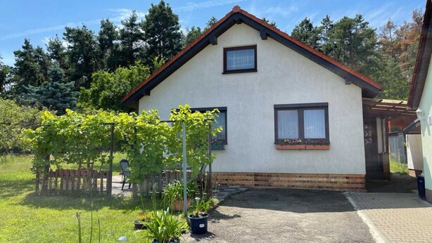 Una casa de un piso con techo inclinado, un pequeño porche y entrada de grava.