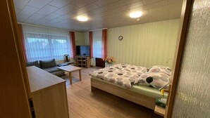 Un espacio habitable compacto con sofá, una mesita, una cama con ropa de cama estampada, un televisor y un reloj en la pared.