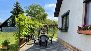 Un patio con mesa y sillas, una pérgola con plantas trepadoras y una casa con jardineras.