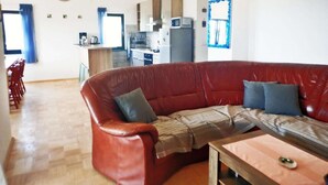 Una sala de estar con un sofá de cuero rojo, una mesa de centro de madera y una cocina al fondo.