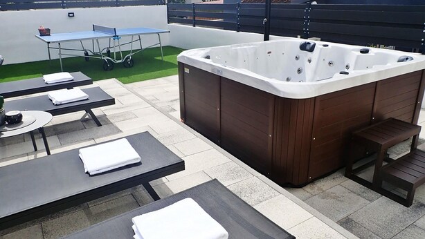 En udendørs terrasse med jacuzzi, borde og stole.